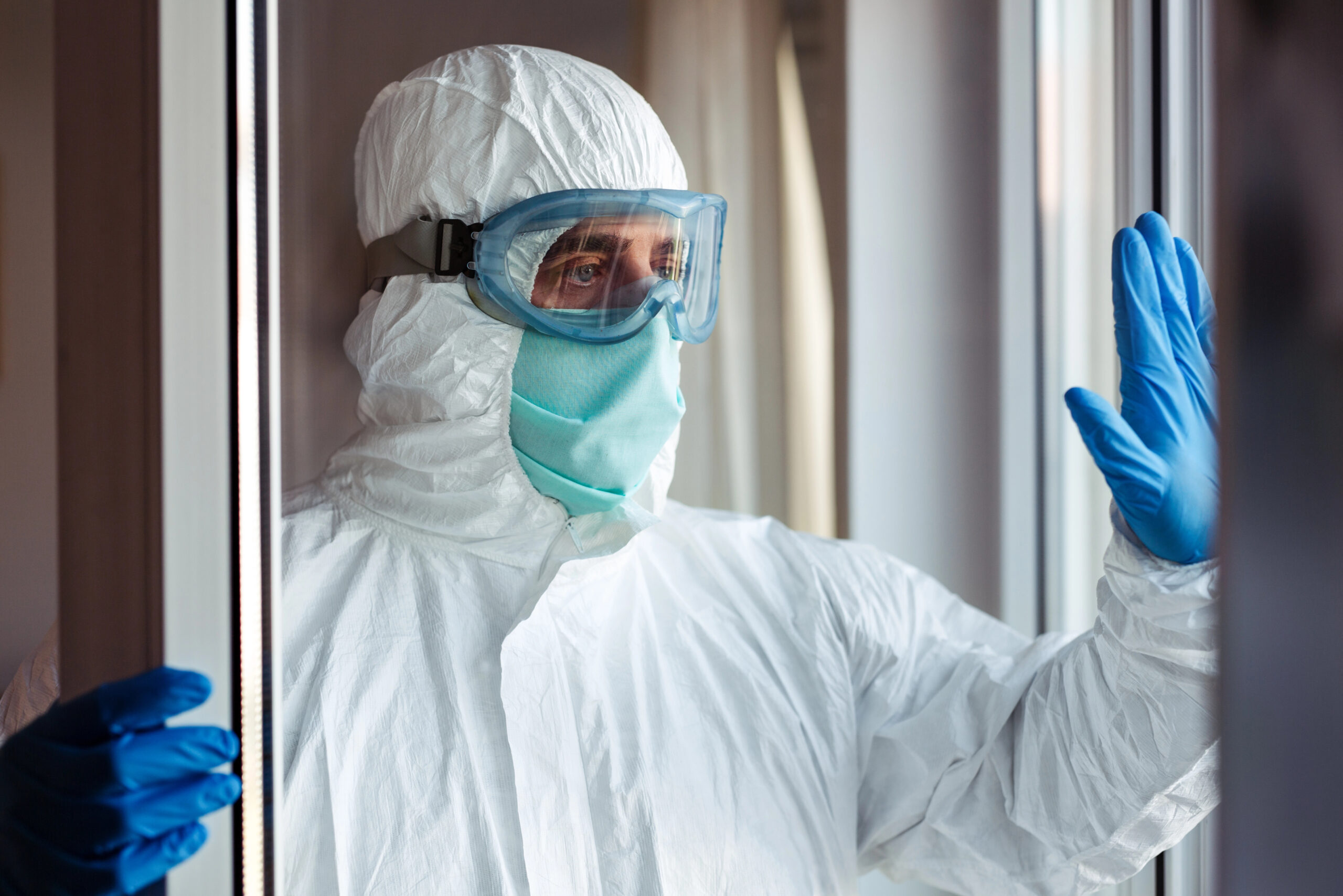 Professional cleaner wearing hazmat suit and blue gloves at trauma scene